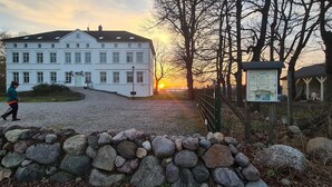 Ein großes, weißes Gebäude mit vielen Fenstern, einer Schotterauffahrt und einer Steinmauer im Vordergrund.