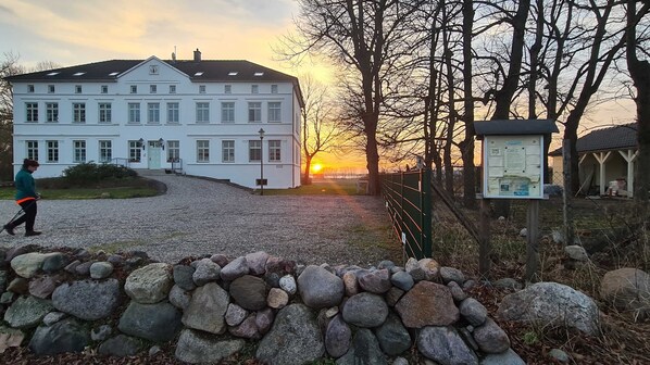 A large white building with multiple windows, a gravel driveway, and a stone wall in the foreground.