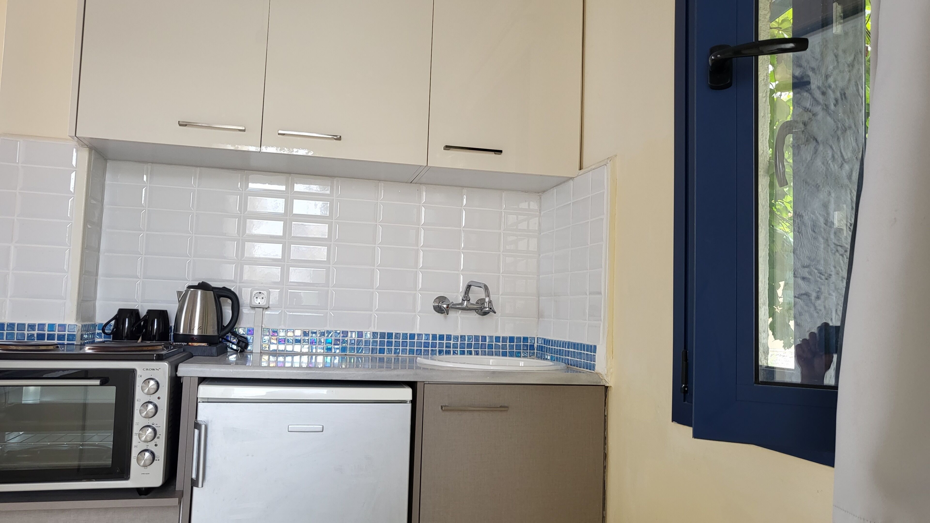 A compact kitchen with white cabinets, a stainless steel kettle, a toaster oven, and a sink.