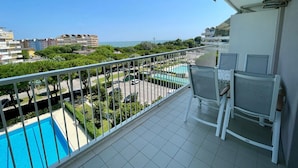 A balcony with a view of a swimming pool, a parking area, and surrounding buildings. - Relax in a our Pool View Apartment (Caorle)