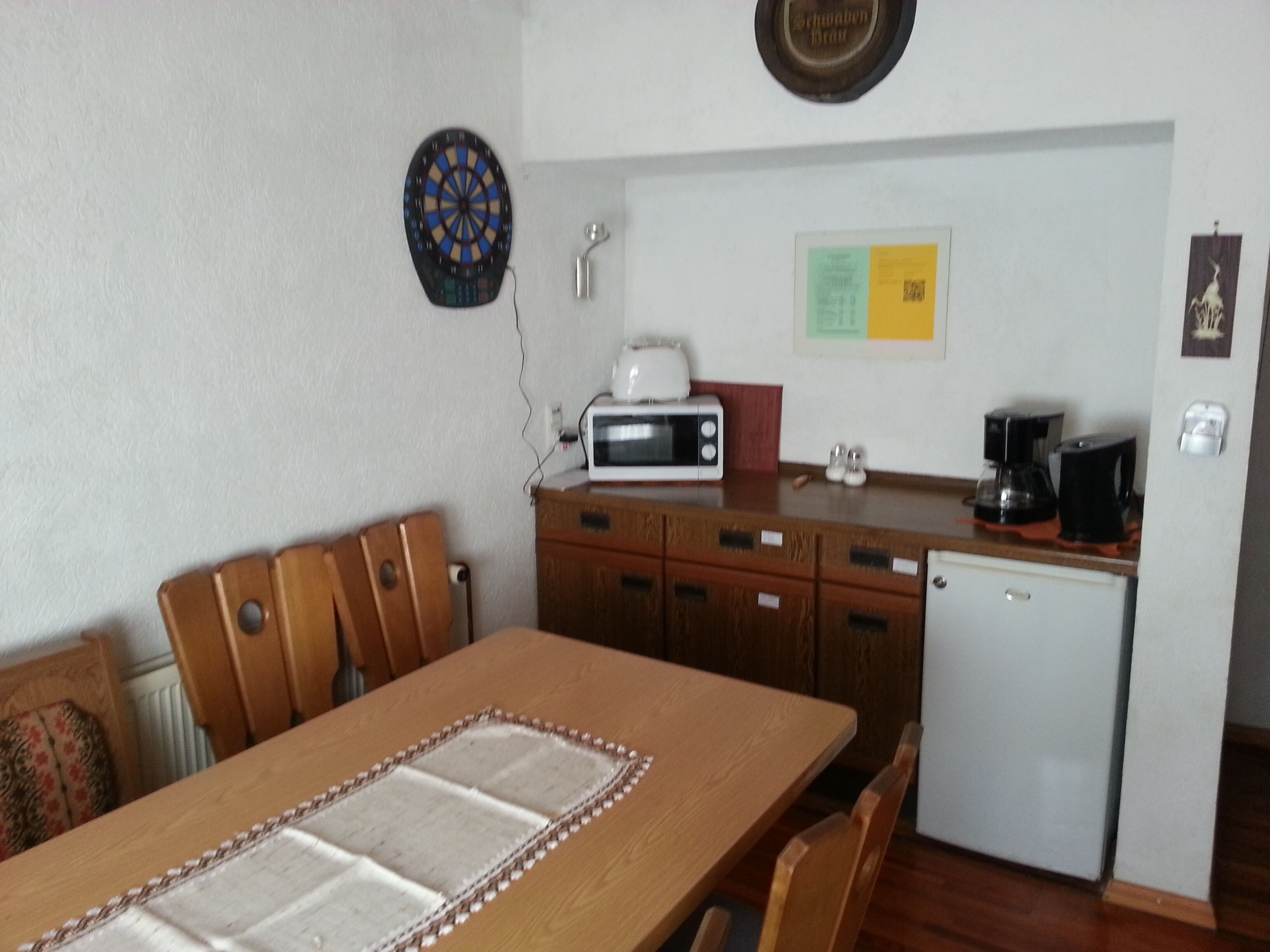 Un comedor con mesa y sillas de madera, microondas, cafetera y refrigerador.