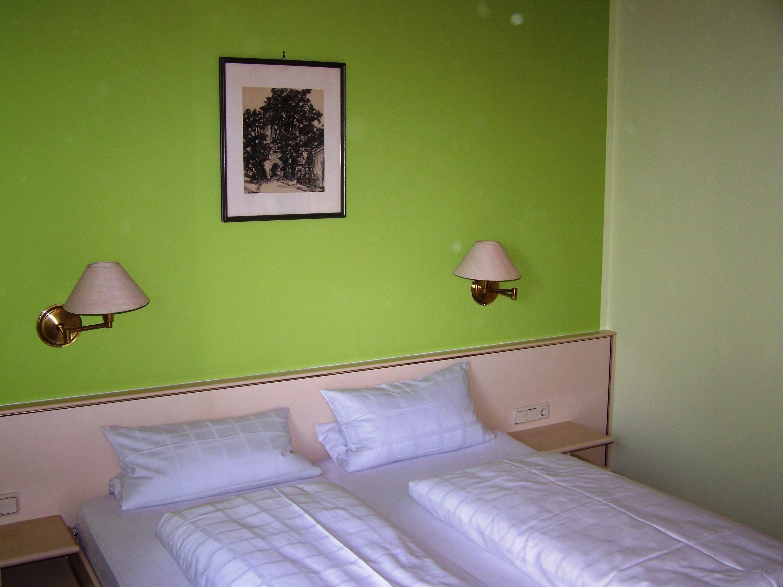 A hotel room with a green wall, two bedside lamps, a framed picture, and a bed with white bedding.