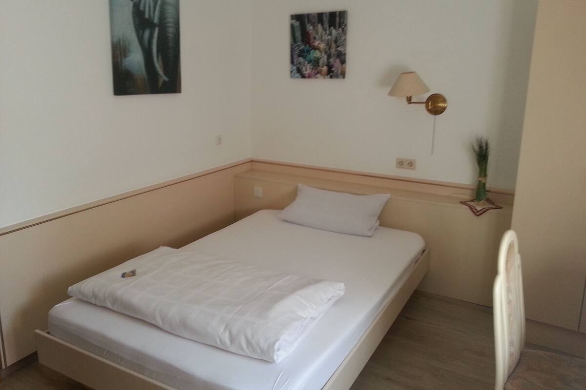 A single bed with white bedding in a room with white walls, a small table, and two wall-mounted lamps.