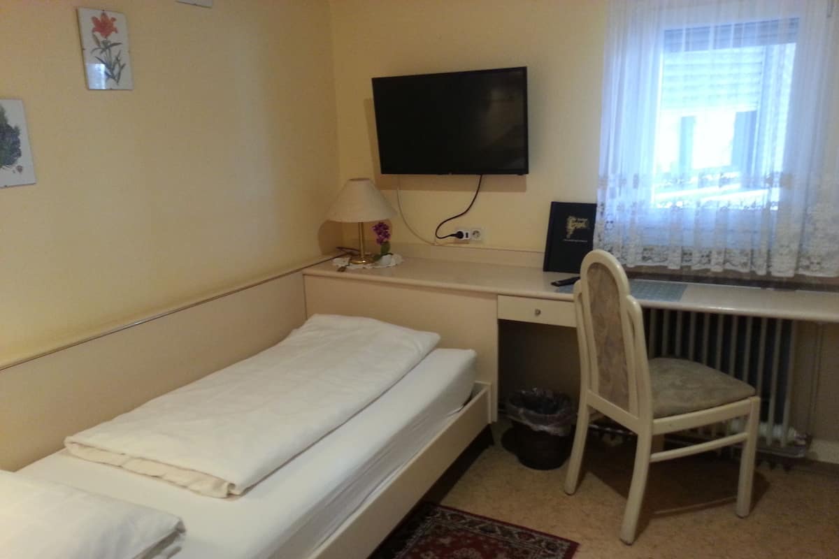 A small, single-bed room with a desk, chair, and a television mounted on the wall.