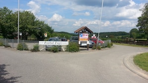 Un área de estacionamiento con un cartel para Gasthof Engelsteinbach, un edificio de techo rojo y un área cercada con coches.