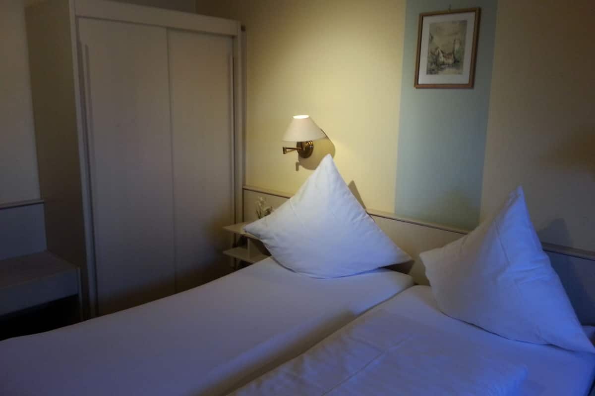 A hotel room with a bed, pillows, a nightstand, a lamp, and a wardrobe.