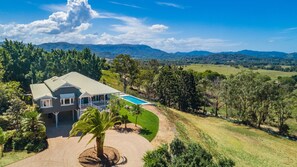 Una casa grande con piscina, rodeada de exuberante vegetación y colinas.