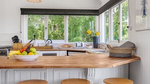 A kitchen with a wooden island, white cabinets, and a large window overlooking greenery. - The Hideout House - hinterland views for miles! (Myocum)