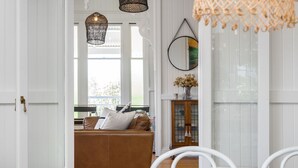 A spacious living room with a brown leather sofa, a wooden cabinet, and a dining area with white chairs. - The Hideout House - hinterland views for miles! (Myocum)