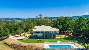 A two-story house with a green roof, surrounded by lush greenery and a swimming pool. - The Hideout House - hinterland views for miles! (Myocum)