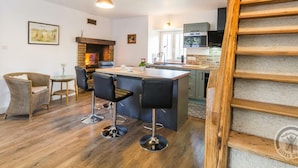 Una cucina moderna con isola centrale, sgabelli da bar, camino e una scala in legno.