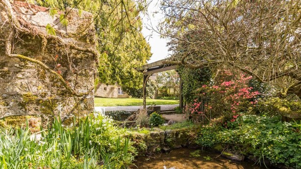 Un giardino con un piccolo stagno, mura in pietra e un ponticello in pietra.