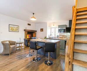 Une cuisine moderne dotée d’un îlot central, de tabourets de bar, d’une cheminée et d’un escalier en bois.