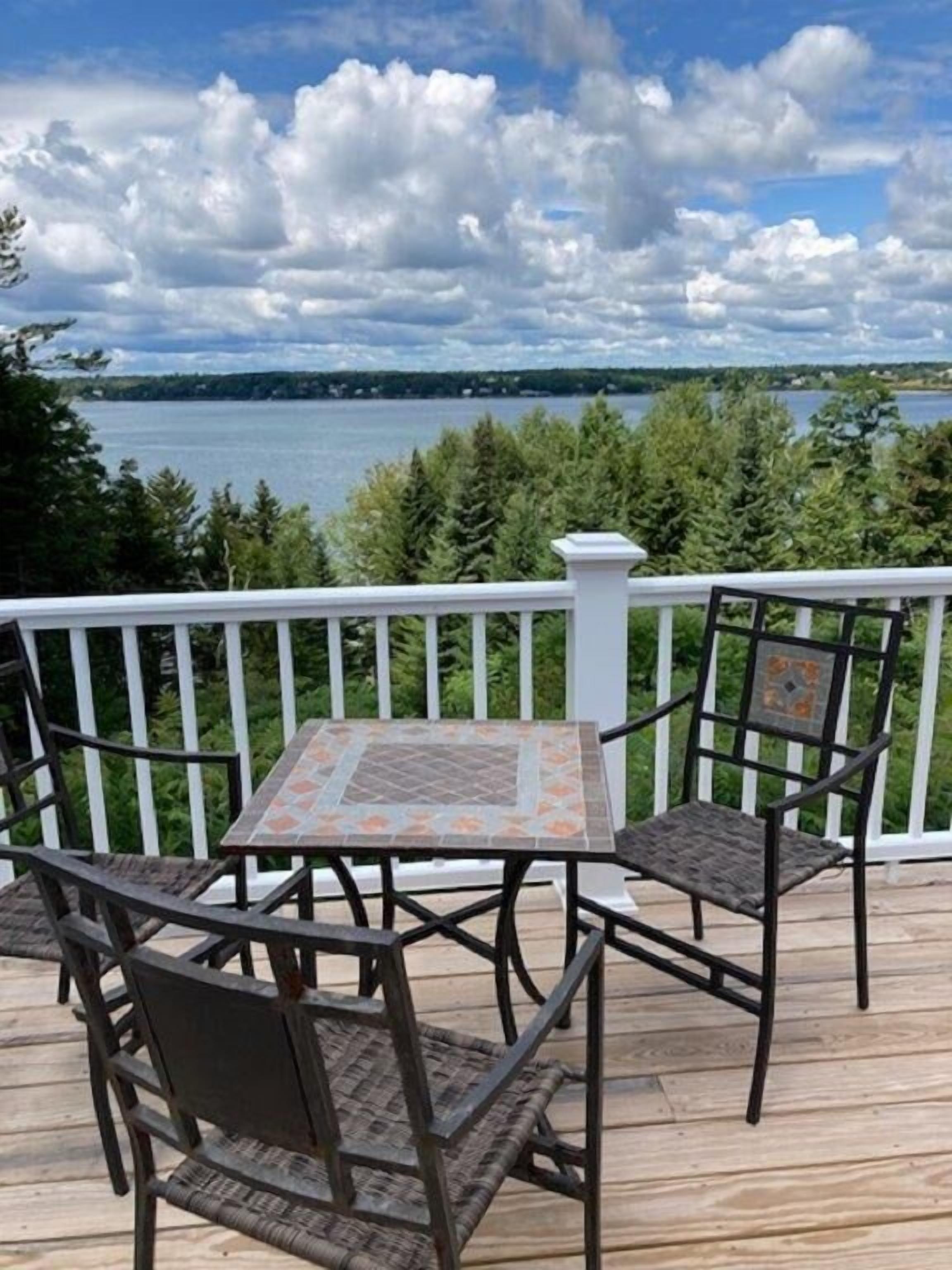 Une terrasse avec une table et des chaises, donnant sur un lac et entourée d’arbres.
