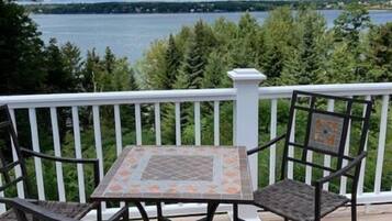 Une terrasse avec une table et des chaises, donnant sur un lac et entourée d’arbres.