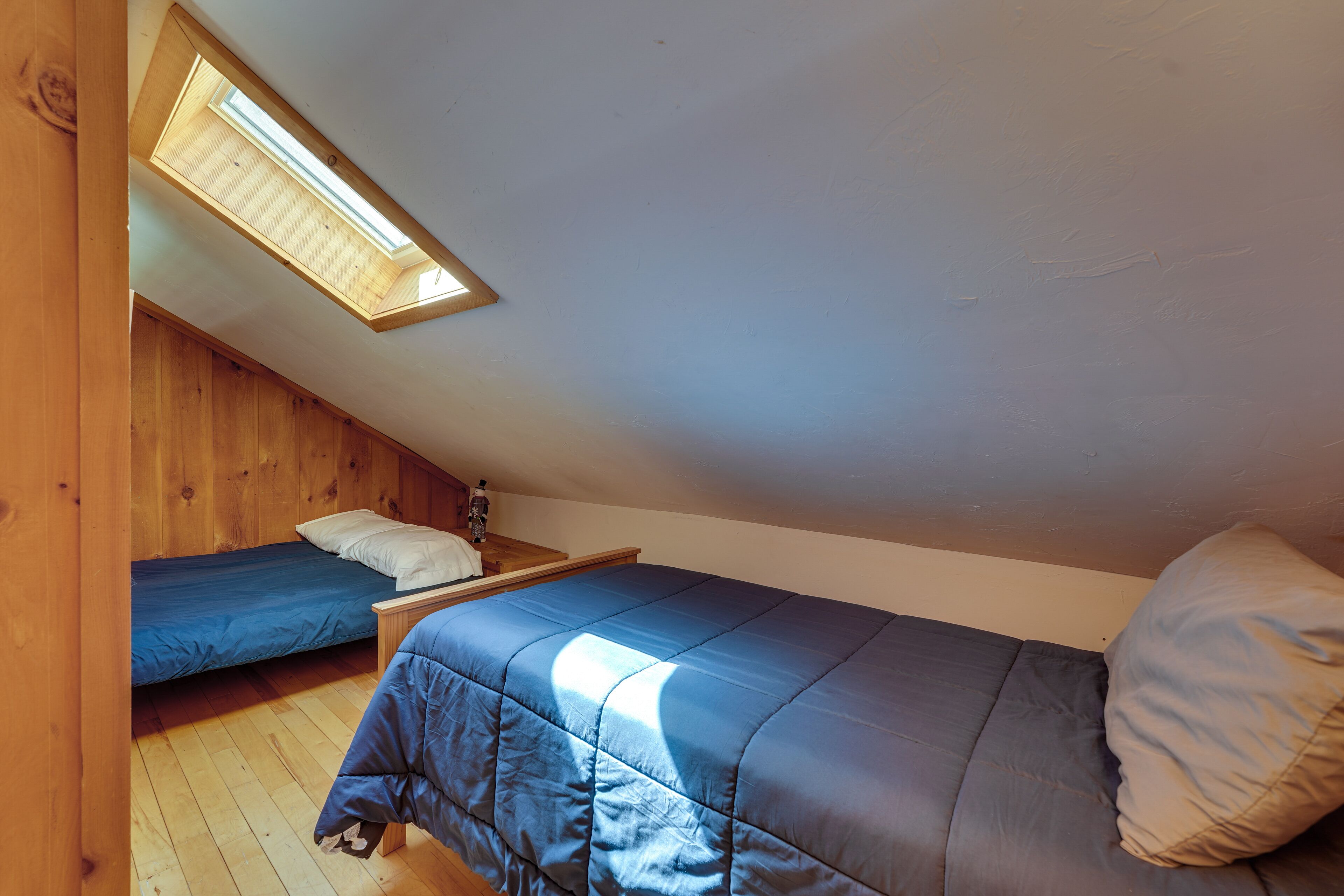Une chambre avec deux lits, des murs en bois, une lucarne et un plancher en bois.