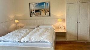 Quarto com cama, duas luminárias de cabeceira, mesa de cabeceira, quadro na parede e guarda-roupa.