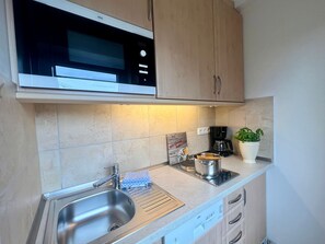 A kitchen with a stainless steel sink, a microwave, a coffee maker, and a potted plant.