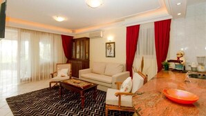 A modern living room with a sofa, armchairs, a coffee table, and a kitchen area with a granite countertop and red decorative bowl. - Milans Apartments (Pržno)