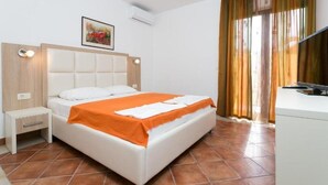 A hotel room with a bed, a nightstand, a desk, and a window with curtains. - Milans Apartments (Pržno)