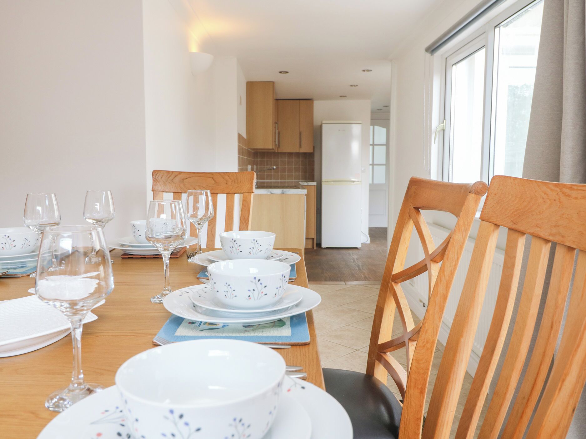 A dining area with a wooden table set for four, including wine glasses and plates.