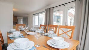 Une table à manger dressée avec de l’assiette blanche, des bols et des verres à vin, entourée de chaises en bois.