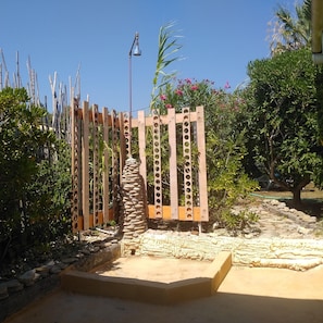 Ein hölzernes Tor mit kreisförmigen Ausschnitten, umgeben von einem Garten mit verschiedenen Pflanzen und einem Palmenbaum.