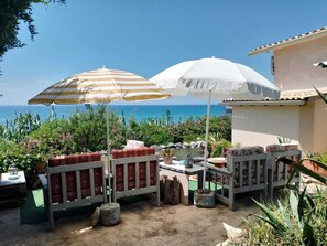 A patio with two striped umbrellas, a wooden bench, and a table with chairs.