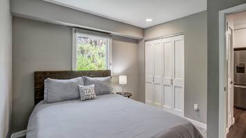 Un dormitorio con una cama, una mesita de noche, un ventanal, un armario y una puerta.