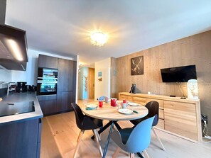 A modern kitchen with a built-in oven, a dining area with a round table and chairs, and a TV mounted on the wall.