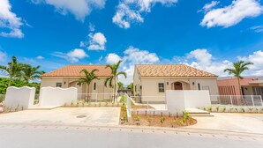 A two-story building with a tiled roof, a gated entrance, and a small garden area with young plants. - Villa Capri Miyakojima (Miyakojima)