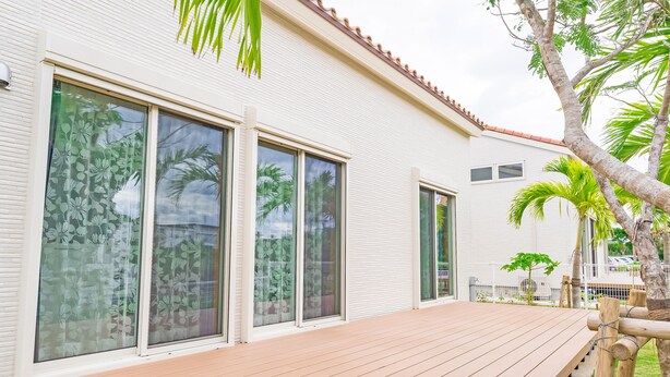 A modern house with large windows, a wooden deck, and a small garden with palm trees. - Villa Capri Miyakojima (Miyakojima)