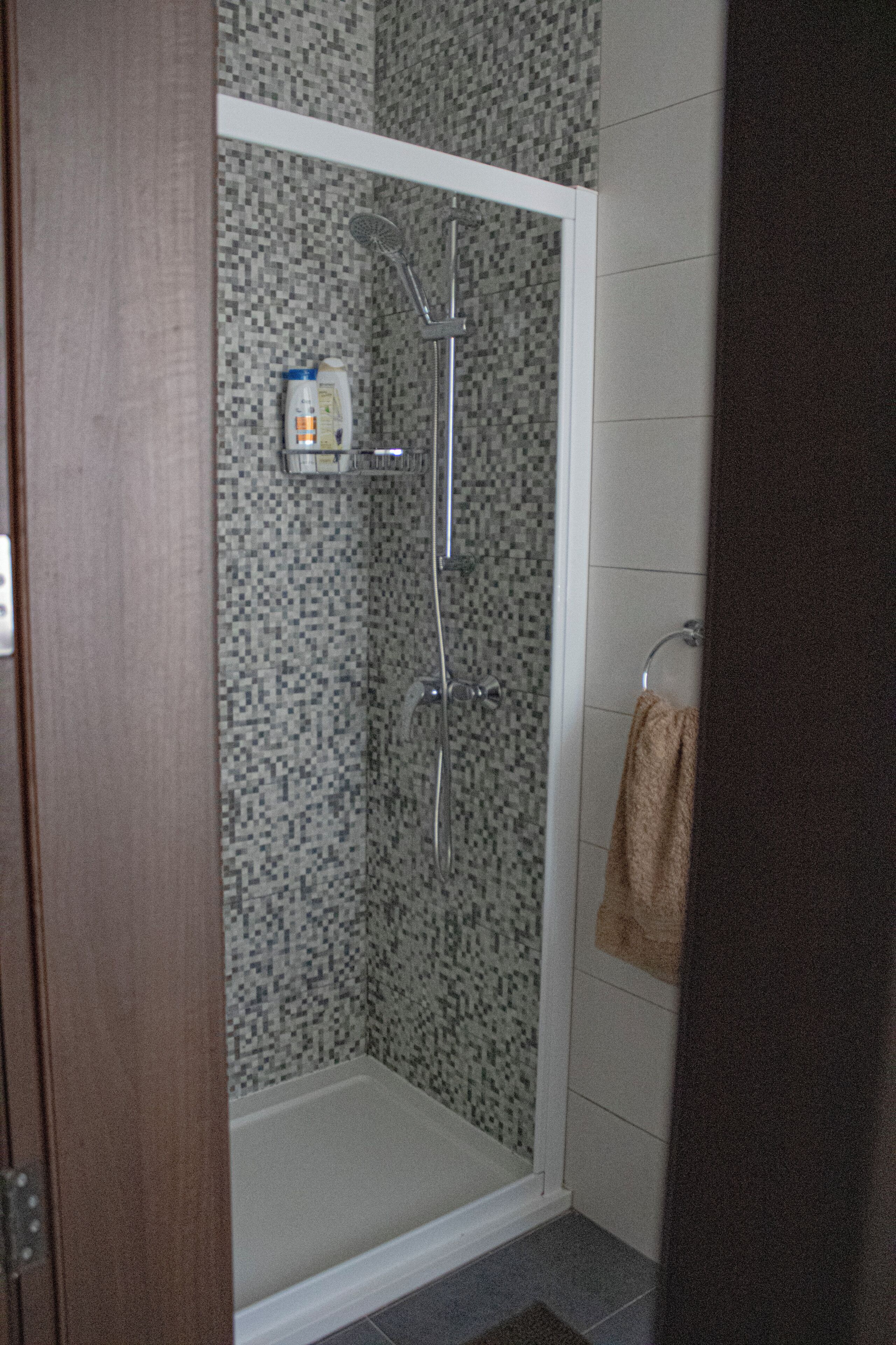 Une douche avec un mur carrelé, un pommeau de douche à main et une bouteille de shampoing.