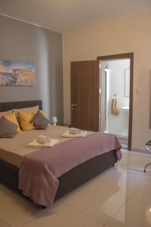 Ein Schlafzimmer mit Bett, Kissen, Nachttisch, einer Tür und einem durchgegangenen Tür sichtbaren Badezimmer.