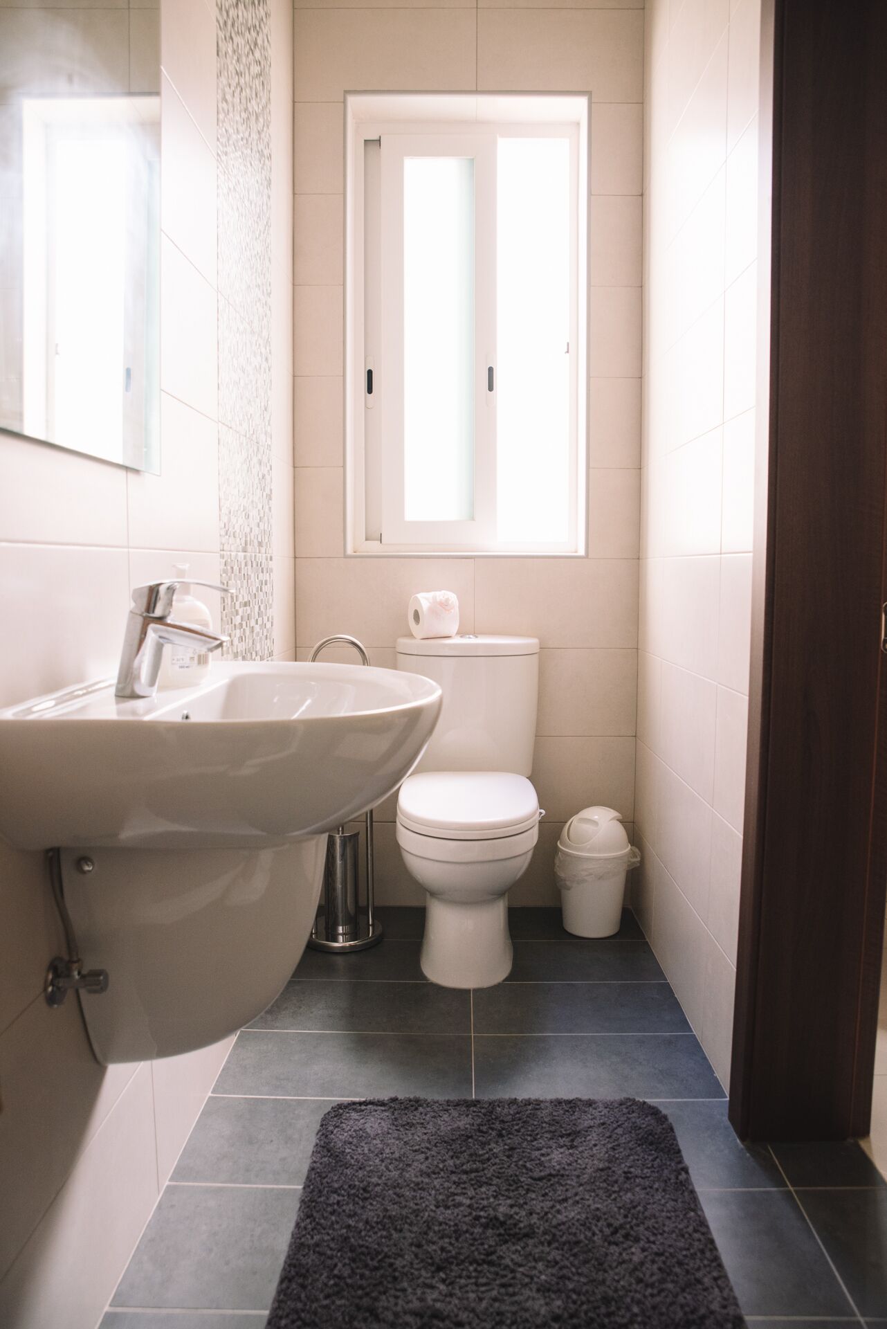 A bathroom with a white sink, toilet, and a window above the toilet.