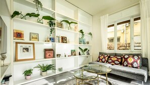 A living room with a sofa, two glass-top coffee tables, a patterned rug, and a white shelving unit with various decorative items and plants. - Serene Retreat with Lush Garden by Sea N Rent (Tel Aviv)