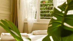 A neatly made bed with white linens and two rolled towels, a window with a view of greenery, and a plant in the foreground. - Serene Retreat with Lush Garden by Sea N Rent (Tel Aviv)