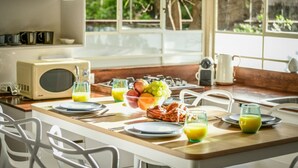 A breakfast setup with a fruit bowl, plates, and glasses of orange juice on a wooden table. - Serene Retreat with Lush Garden by Sea N Rent (Tel Aviv)