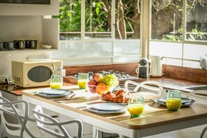 Une table en bois dressée pour le petit-déjeuner, avec un four à micro-ondes, un panier de fruits et des verres de jus d’orange.
