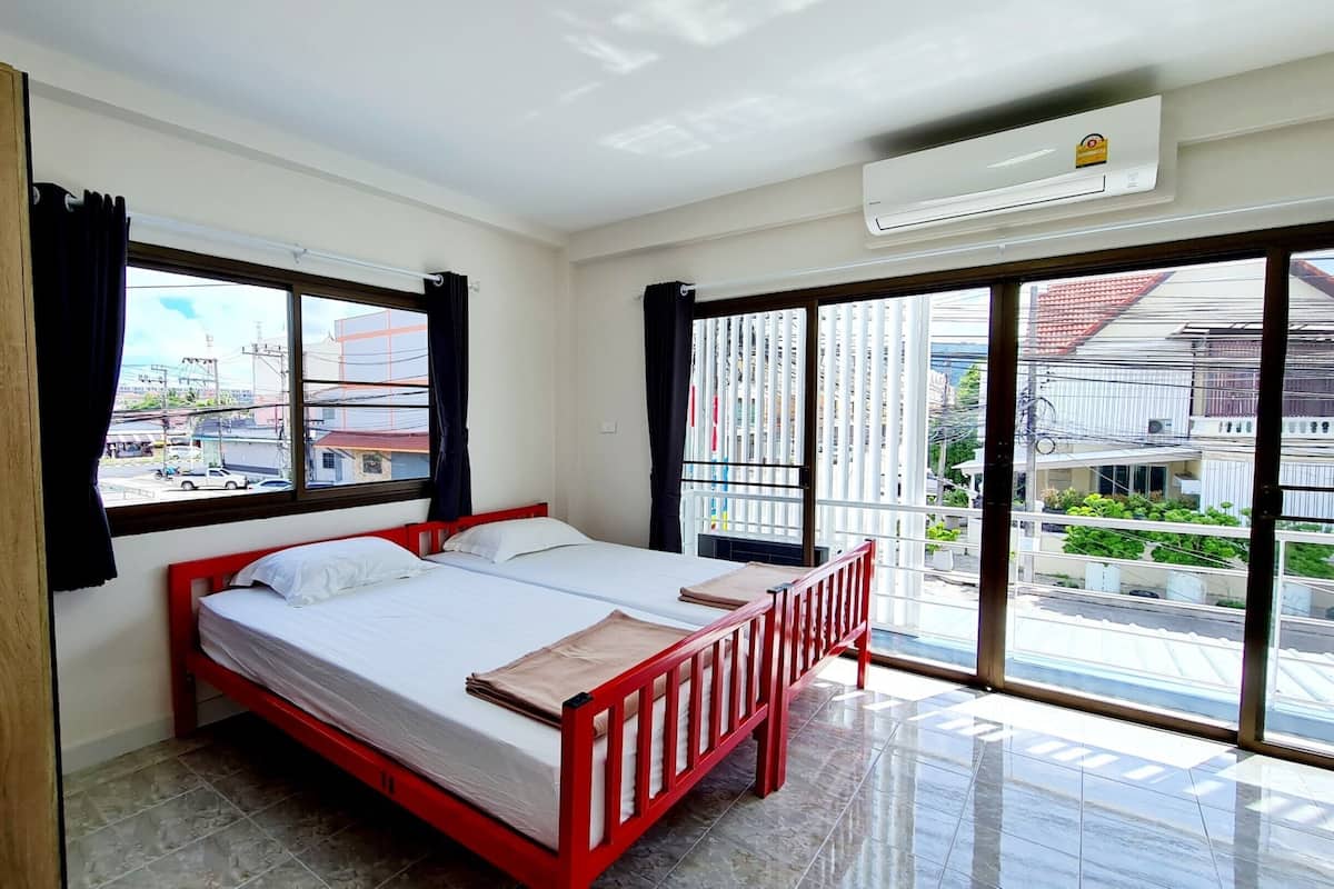 A hotel room with a bed, a window with curtains, an air conditioning unit, and a view of the street outside.