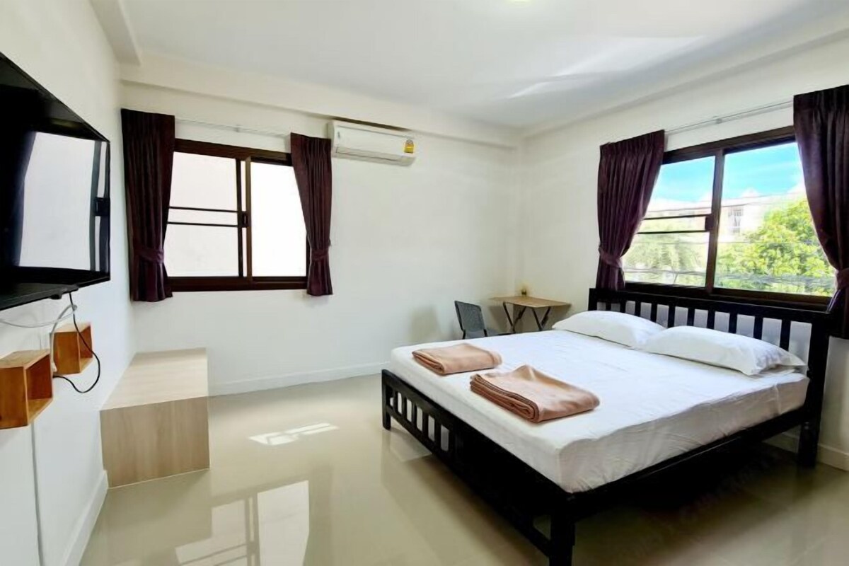Une chambre d’hôtel moderne avec un grand lit, un téléviseur à écran plat fixé au mur, une petite table et une fenêtre avec des rideaux.
