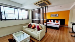 A modern hotel room with a sofa, a bed, a glass coffee table, and a large window with blinds. - TP House @town (Phuket)