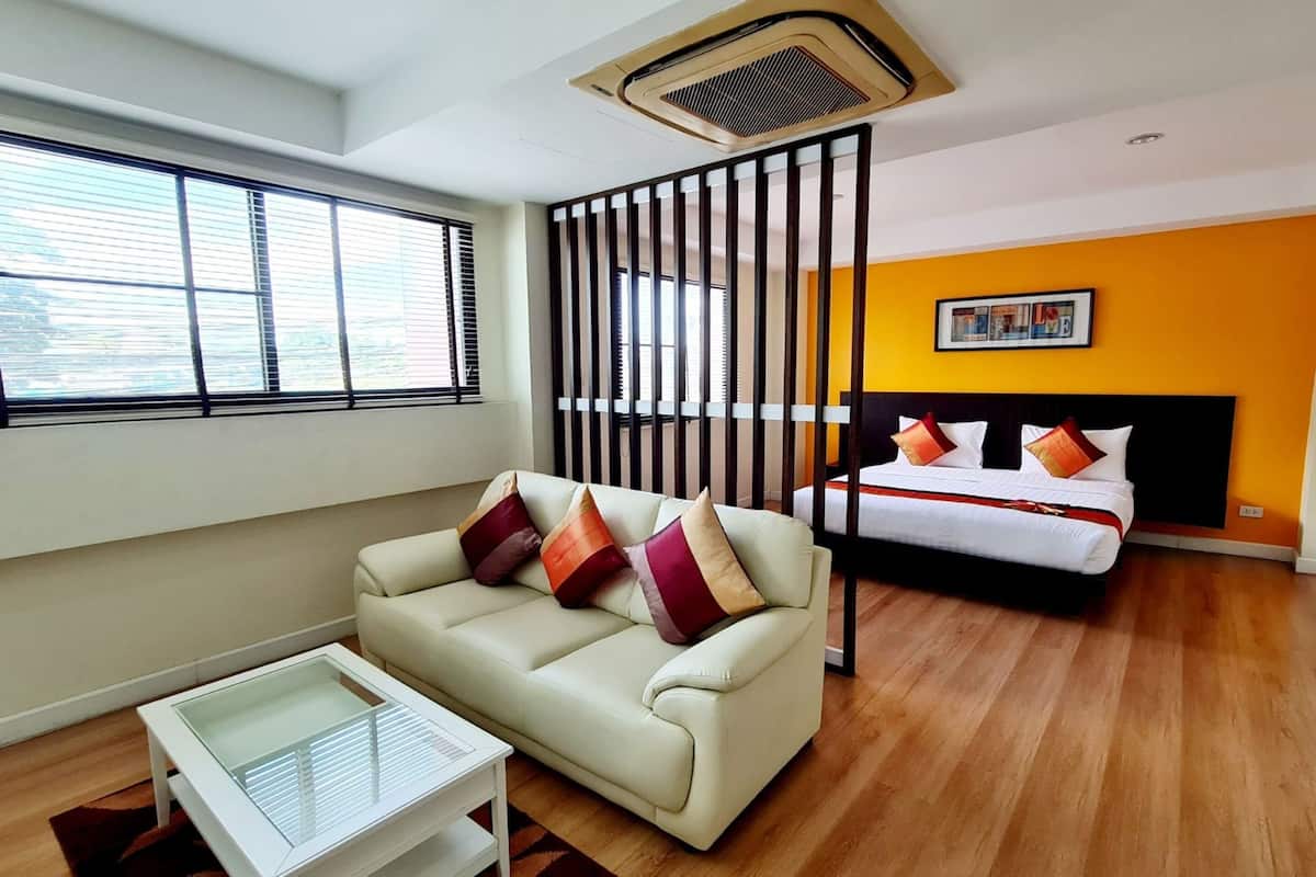 A modern hotel room with a sofa, a bed, a glass coffee table, and a large window with blinds.