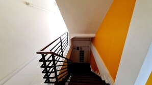 A staircase with black railings and a white wall on one side and an orange wall on the other. - TP House @town (Phuket)