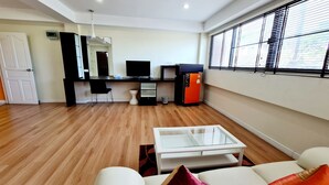A modern living room with a white sofa, a glass coffee table, and a kitchen area with a refrigerator, stove, and sink. - TP House @town (Phuket)