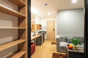 A modern living room with a grey sofa, a wooden bookshelf, and a kitchen area in the background.