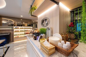 Um hall de hotel moderno com uma recepção de mármore, uma obra de arte de globo mural e diversas comodidades, incluindo um espaço para café e um arranjo de plantas.