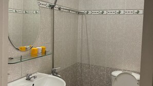Kylpyhuone, jossa on pesuallas, peili, wc, suihku ja kuviollisia laattoja.