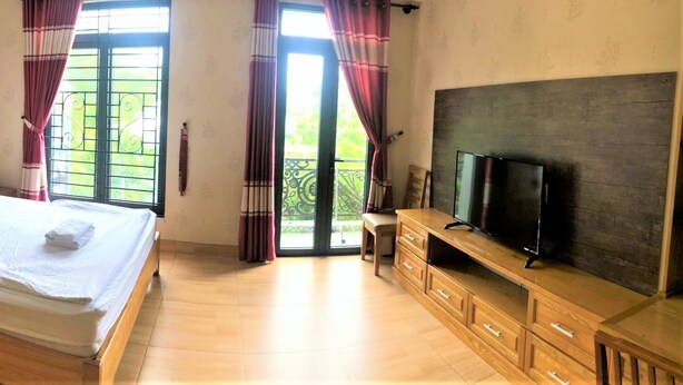 Ein Schlafzimmer mit einem Bett, einem Fernseher auf einem Holztisch und einem Balkon mit Vorhängen.