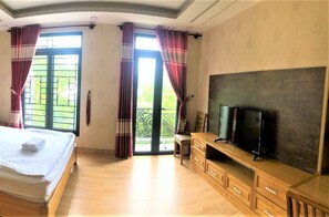 A bedroom with a bed, a TV on a wooden stand, and a balcony with curtains.